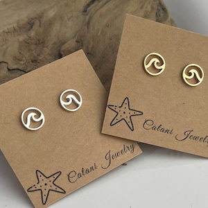 May include: Two pairs of wave-shaped stud earrings, one silver and one gold, displayed on brown cards. The cards feature a starfish graphic and the text "Catani Jewelry". The earrings are small and circular, with a cutout wave design.