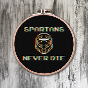 Könnte beinhalten: Ein schwarzer Stickrahmen mit dem Text "SPARTANS NEVER DIE" in regenbogenfarbener Pixel-Schrift. In der Mitte des Rahmens befindet sich ein Pixelbild eines spartanischen Helms.