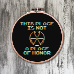 May include: A black embroidery hoop with white text that reads "This place is not a place of honor" and a pixelated symbol in the center.
