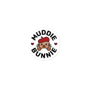 Könnte beinhalten: Ein runder Aufkleber mit einem Cartoon-Hasen, der einen roten Barett trägt. Der Hase ist braun mit schwarzen Schnurrhaaren und einer kleinen rosa Nase. Der Text "Muddie Bunnie" ist in schwarzer, kreisförmiger Schrift um den Hasen herum, mit roten Herzen auf beiden Seiten.