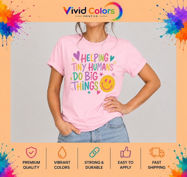 May include: A light pink short-sleeve t-shirt featuring the multi-colored text HELPING TINY HUMANS DO BIG THINGS. The design includes a yellow smiley face, small purple and teal hearts, and star accents printed on the front of the garment.