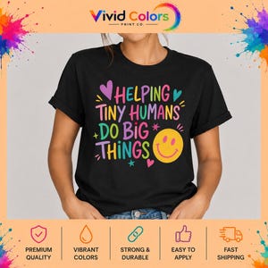 May include: A black short-sleeved t-shirt featuring the colorful text HELPING TINY HUMANS DO BIG THINGS in a mix of pink, yellow, blue, and purple fonts. The design includes small star and heart accents along with a large yellow smiley face icon.