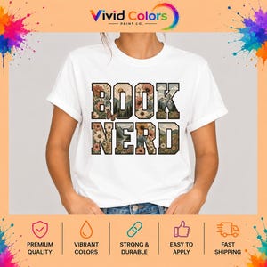 May include: A white short-sleeved t-shirt featuring the text BOOK NERD in large block letters. The letters are filled with a graphic design of colorful flowers, green mountains, a sun, and a small brown butterfly on a light background.