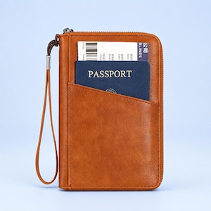 May include: A tan travel wallet with a zippered closure and a wrist strap. The front features a pocket containing a dark blue passport and a white airline boarding pass with a visible barcode and the text AIRLINES printed on the side.