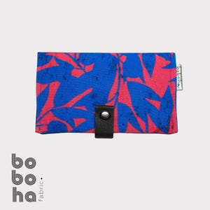 May include: A rectangular wallet featuring a vibrant blue and pink leaf pattern. The wallet is secured with a black leather-like tab and a silver metal snap button. A small white fabric tag with the text boboha is attached to the right side.