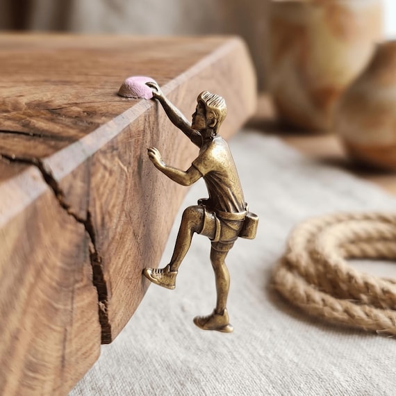 A tiny brass rock climber figurine that magnetically grips any surface edge — miniature sculpture that's all personality and zero wasted space.