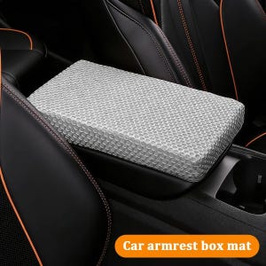 Puede incluir: Una alfombrilla gris y texturizada para la caja del reposabrazos del coche. La alfombrilla es rectangular y se coloca sobre el reposabrazos de la consola central del coche. Los asientos de cuero negro del coche tienen costuras naranjas. El texto "Car armrest box mat" está en la esquina inferior derecha.