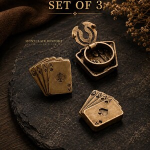 May include: Set of 3 antique brass playing card-themed items. Includes a hinged ring box and two sets of four miniature playing cards, each showing the Ace of Spades. The text "SET OF 3" and "MONTCLAIR BESPOKE" are visible.