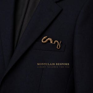 Puede incluir: Un blazer azul marino oscuro con un pin de solapa de serpiente dorada en el bolsillo. El texto "MONTCLAIR BESPOKE LUXURY TAILORED FOR YOU" está impreso en dorado.