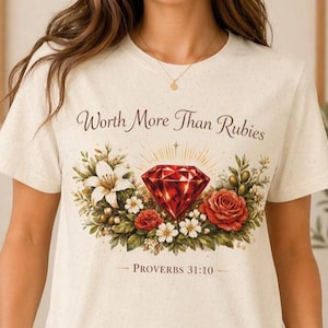 Puede incluir: Camiseta color crema con un gráfico de una gema roja rodeada de flores y follaje. El texto "Worth More Than Rubies" y "Proverbs 31:10" están impresos encima y debajo del gráfico. La camiseta la lleva una persona.