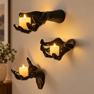 May include: Three black wall-mounted hand sculptures, each featuring an open palm design that holds a single white cylindrical candle. The hands are finished with a glossy sheen and are positioned at varying heights on the wall, with each candle emitting a warm, soft glow.