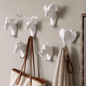 Può includere: Ganci da parete a forma di testa di animale bianchi, tra cui una giraffa, un cervo, un ariete, un elefante, un cavallo e un rinoceronte. Una borsa tote beige con manici marroni è appesa al gancio del cavallo. Una sciarpa e delle chiavi sono appese al gancio dell'elefante.