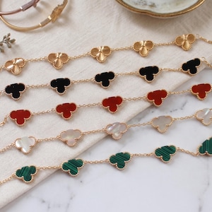 Puede incluir: Pulseras de cadena doradas con abalorios en forma de trébol en varios colores: dorado, negro, rojo, blanco y verde. Las pulseras se exhiben sobre una superficie clara, mostrando su delicado diseño y artesanía.