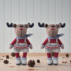 Op de afbeelding: Twee handgemaakte gehaakte rendierpoppen. Elke pop heeft een bruin hoofd met donkerblauwe geweien, een rode trui, grijze shorts met een wit en rood patroon en witte laarzen. Ze dragen een lichtblauwe sjaal. Pijnappels zijn verspreid.