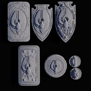 Puede incluir: Una colección de esculturas en relieve grises y ornamentadas que presentan un diseño central de ave con las alas extendidas. Las piezas varían en forma, incluyendo formas rectangulares, en forma de escudo y circulares, con detalladas borduras florales y geométricas. El fondo es negro.