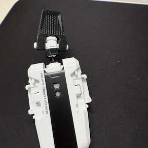 Può includere: Un lanciatore a corda Beyblade X bianco e nero con un'impugnatura nera testurizzata. Il dispositivo presenta un pannello centrale nero con il testo BEYBLADE X STRING LAUNCHER stampato verticalmente in bianco sul lato sinistro dell'involucro in plastica.