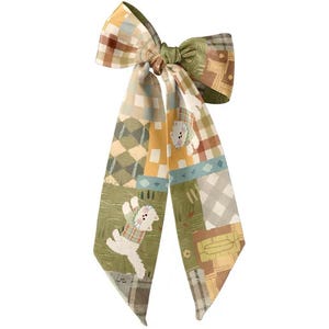 Op de afbeelding: Een decoratieve haarstrik met een patchwork-ontwerp in groen, geel en bruin. De strik heeft een herhalend patroon van geometrische vormen en een cartoonhond. De tekst "YYXaccessory" staat onderaan.