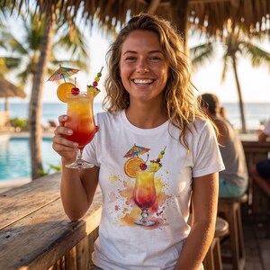 Könnte beinhalten: Ein weißes T-Shirt mit einer farbenfrohen Aquarellgrafik eines tropischen Cocktails in einem Hurricane-Glas, garniert mit einer Orangenscheibe, einer Kirsche, einem Ananasstück und einem kleinen Papierschirmchen, passend zum Getränk in der Hand.