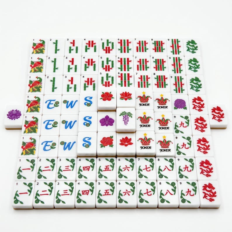 May include: A set of white Mahjong tiles arranged in a grid, featuring various colorful illustrations including red birds, green bamboo, blue directional letters, red Chinese numerals, floral patterns, dragon motifs, and Joker tiles with colorful hats.