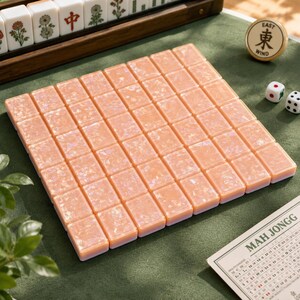 May include: A set of rectangular mahjong tiles with a peach-colored, pearlescent finish arranged in a grid. The set includes two white dice with black dots, a circular token labeled East Wind, and a score card with the text Mah Jongg printed on it.