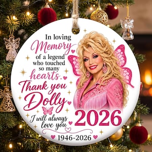 May include: A round white ceramic ornament featuring a portrait of Dolly Parton with pink butterfly wings. The text reads: In loving Memory of a legend who touched so many hearts. Thank you Dolly I will always love you 2026 1946-2026.