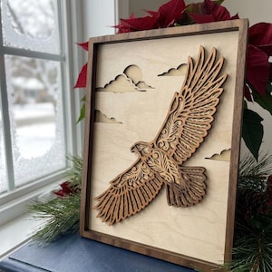 Puede incluir: Obra de arte mural de madera con un águila en vuelo cortada con láser. El águila marrón, con detalles de plumas, se destaca sobre un fondo claro con nubes recortadas. La obra está enmarcada en madera marrón oscuro. Dimensiones: aprox. 30 cm x 40 cm.