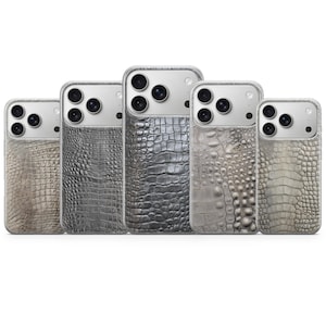 Pode incluir: Cinco capas de telemóvel com textura de pele de crocodilo em tons de cinza e bege. As capas têm uma borda transparente e um recorte para a câmara. As capas estão dispostas em fila, mostrando as diferentes variações de cor.