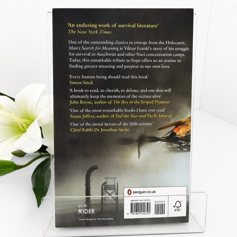May include: A book cover for "Man's Search for Meaning" by Viktor Frankl, displayed in a clear acrylic stand. The cover features text from The New York Times and other authors. The book's cover has a dark background with a graphic of a bird and a wheelchair.