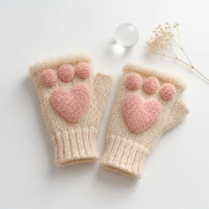 Könnte beinhalten: Ein Paar cremefarbene Fingerhandschuhe mit einem rosa Herz- und Pfotenabdruck-Design. Die gestrickten Handschuhe haben einen weichen, flauschigen Besatz um den Handgelenkbereich.