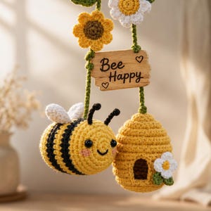 Peut inclure: Décoration suspendue sur le thème des abeilles, faite au crochet. Le design comprend une abeille souriante avec des rayures noires, une ruche et une pancarte en bois avec l'inscription "Bee Happy". La décoration comprend également des fleurs crochetées jaunes et blanches.