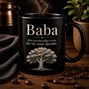 Könnte beinhalten: Schwarze Kaffeetasse mit dem Wort "Baba" in Weiß, türkischem Text und einer Baumillustration. Die Tasse steht auf einer Holzoberfläche, umgeben von Kaffeebohnen.