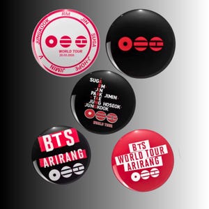 May include: A selection of circular, glossy badges with diverse designs. Some badges display the text "BTS" and "ARIRANG" in white and red. Other badges feature "WORLD TOUR" and band member names. The badges are predominantly black and red.