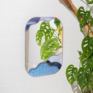Stained glass mirror with blue cloud design hanging near indoor plant