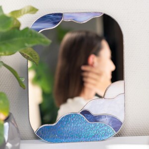 Stained glass cloud mirror reflecting woman in cozy home interior