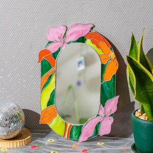 Close up of stained glass floral mirror with pink petals and orange glass details