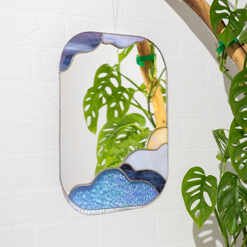 Stained glass mirror with blue cloud design hanging near indoor plant