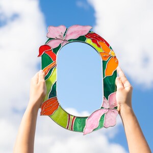 Stained glass floral mirror held in hands against blue sky background