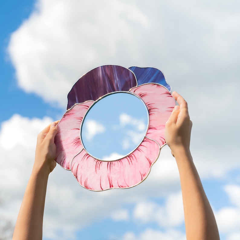 Stained glass pansy mirror held against sky with soft clouds reflection