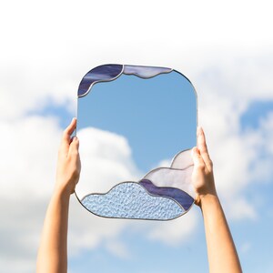 Stained glass cloud mirror held against sky with clouds reflection