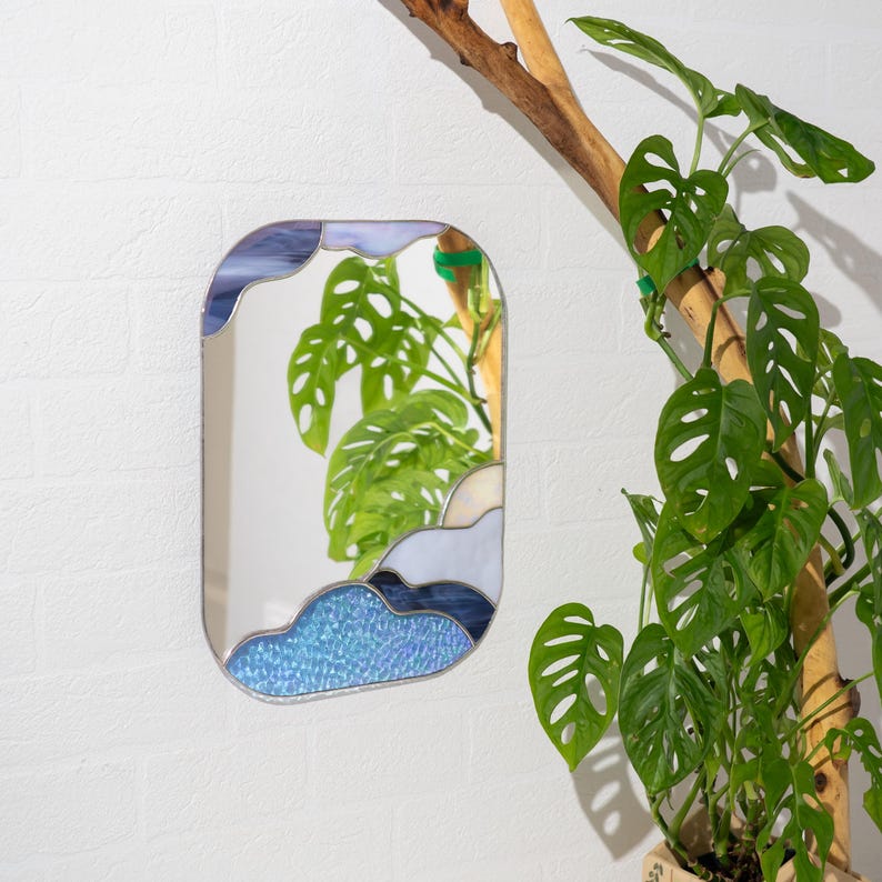 Stained glass mirror with blue cloud design hanging near indoor plant