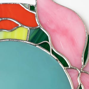 Close up of stained glass floral mirror showing pink petal and green glass details