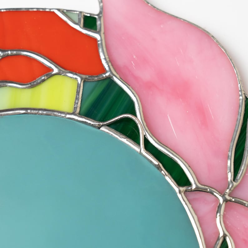 Close up of stained glass floral mirror showing pink petal and green glass details