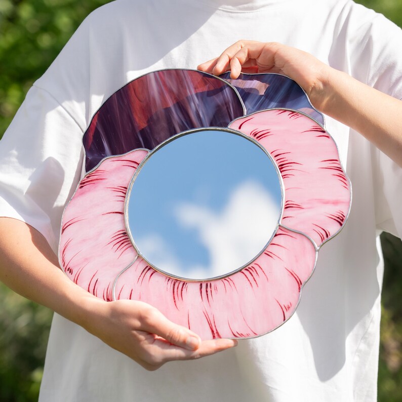 Handmade stained glass pansy mirror held in hands outdoor sunlight