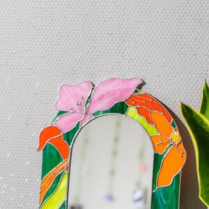 Close up of stained glass floral mirror with pink flower and green glass frame