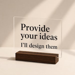 Könnte beinhalten: Ein klares Acrylschild mit dem Text "Provide your ideas I'll design them" in Schwarz. Das Schild wird von einem dunkelbraunen Holzsockel gehalten. Das Schild ist rechteckig und steht aufrecht.