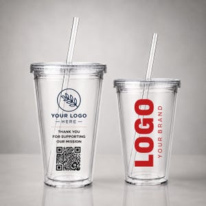 Op de afbeelding: Twee doorzichtige plastic bekers met deksels en rietjes. De linker beker heeft een donkerblauw cirkelvormig logo, de tekst YOUR LOGO HERE, THANK YOU FOR SUPPORTING OUR MISSION en een QR-code. De rechter beker toont de rode tekst LOGO YOUR BRAND.