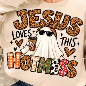 Könnte beinhalten: Ein beigefarbenes Sweatshirt mit Rundhalsausschnitt und einer Grafik eines Geistes, der eine Leopardenmuster-Schleife und eine Sonnenbrille trägt und einen Kaffeebecher hält. Der Text JESUS LOVES THIS HOTMESS ist in Leoparden-, Orange-, Grün- und Rotkaro-Mustern gestaltet.