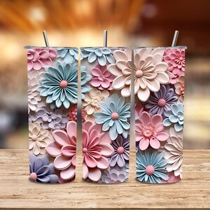 Puede incluir: Tres vasos de acero inoxidable con dise&ntilde;os florales en colores pastel. Las flores son en tonos rosa, azul y crema, con un efecto 3D. Cada vaso tiene una pajita plateada.