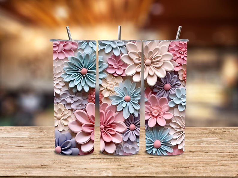 Puede incluir: Tres vasos de acero inoxidable con dise&ntilde;os florales en colores pastel. Las flores son en tonos rosa, azul y crema, con un efecto 3D. Cada vaso tiene una pajita plateada.