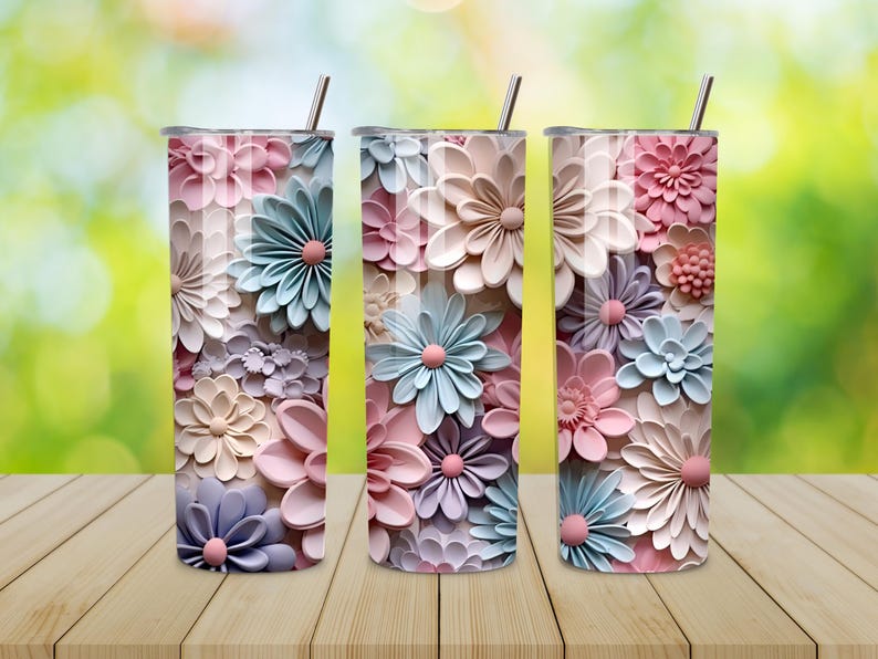 Puede incluir: Tres vasos aislados de acero inoxidable con dise&ntilde;os florales. Los vasos presentan una variedad de flores en colores pastel, rosa, azul y lavanda. Cada vaso tiene una pajita plateada y una tapa. El fondo es verde borroso y los vasos est&aacute;n sobre una superficie de madera.